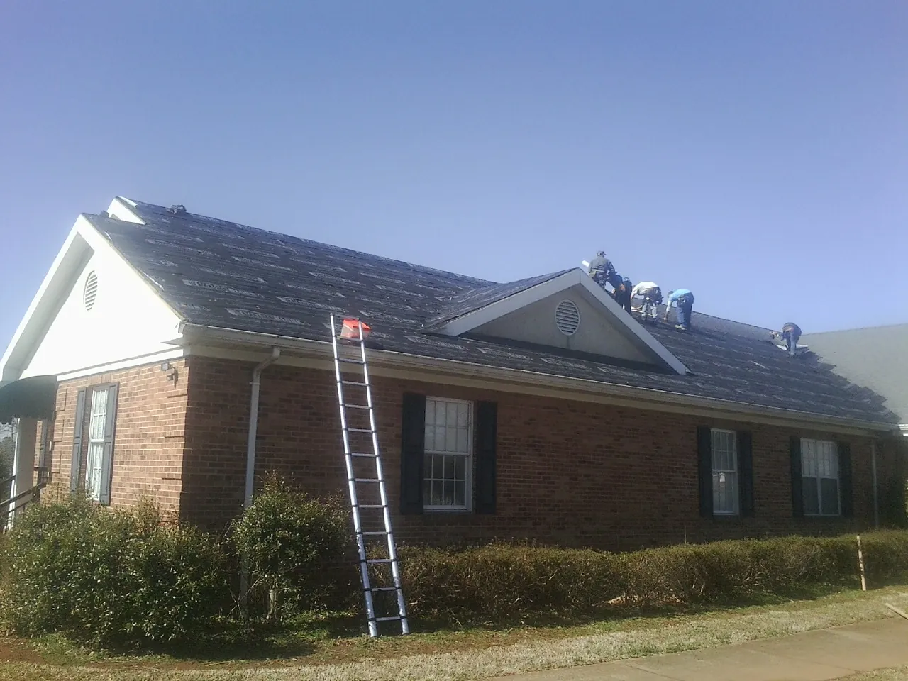 Crew tearing shingles off a brick ranch roof with a ladder set — Emergency Roof Repair work by our crew in Balm
