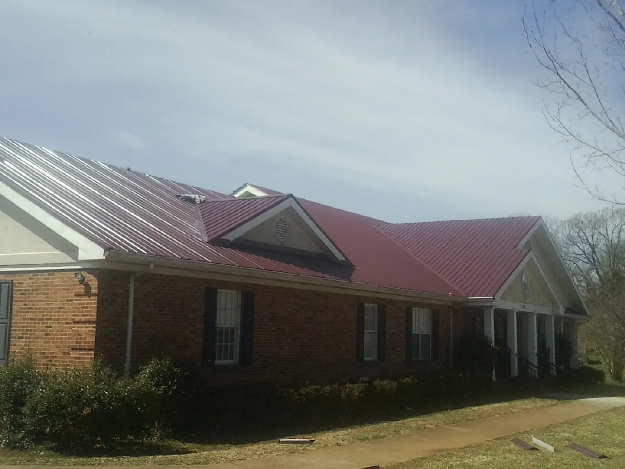 Red metal roof with gabled entries on a long brick building, from a Hail Damage Roof Repair job in Balm