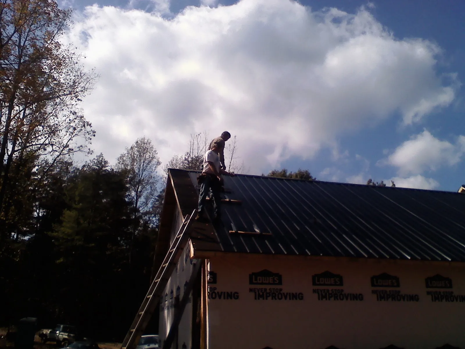 Roofer fastening dark metal panels high against a cloudy sky, from a Roof Inspection job in Balm