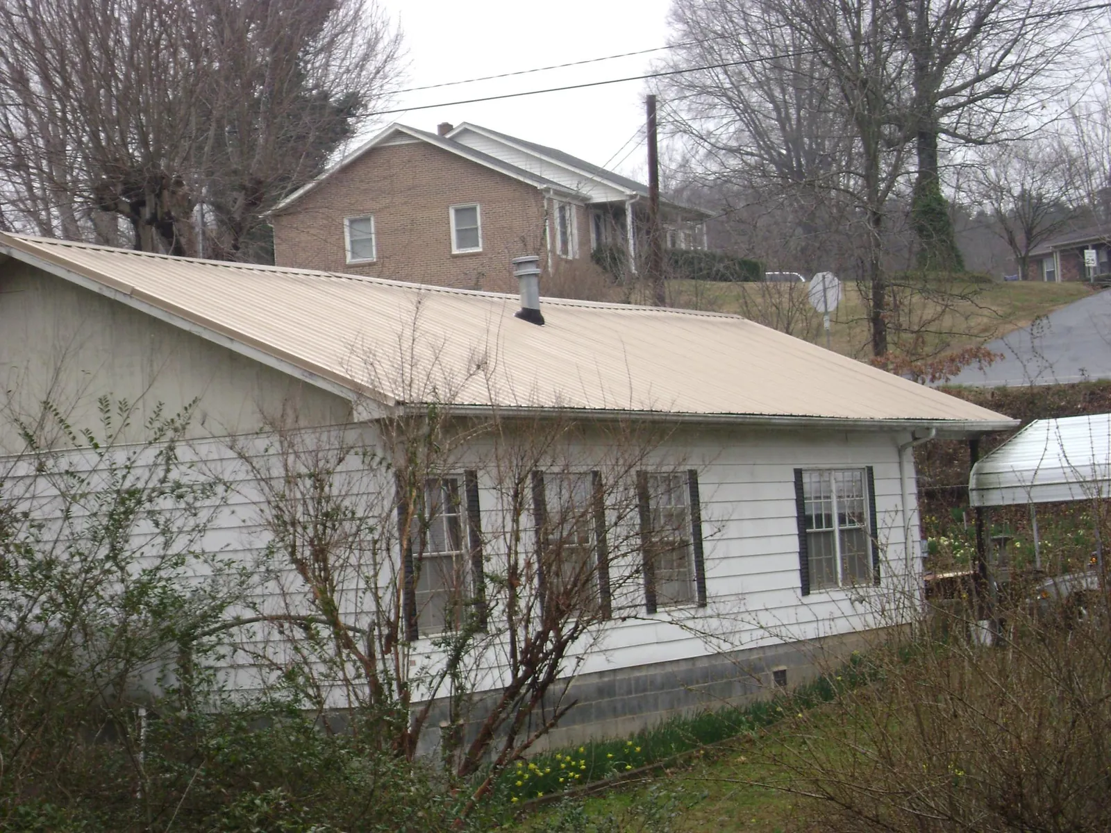 Tan metal roof on a white sided house set into a hillside — Commercial Roofing by Roofing Brothers in Balm